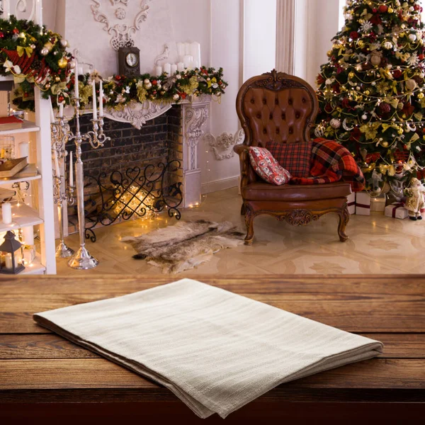 Empty white tablecloth on wooden desk perspective. Festive sparkling Christmas interiors background. Selective focus.