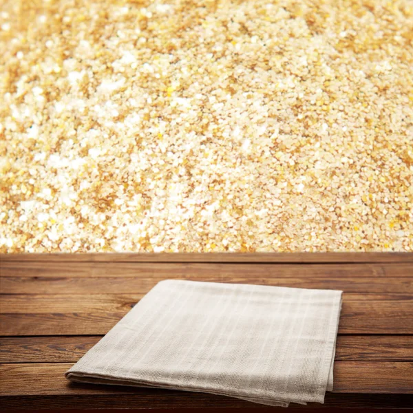 Empty white tablecloth on wooden desk perspective. Festive sparkling gold background. Selective focus.