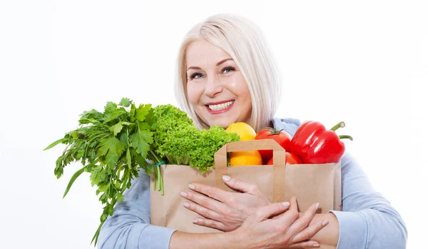 Stock image Happy woman with blond hair and beautiful smile holds a bag of vegetables and herbs red pepper and green lettuce in her hands for a healthy diet with vitaminswith. Concept healthy food vegetable, closeup