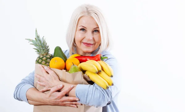Happy middle aged woman with beautiful smile holds many fruits oranges, lemon, bananas, kiwi, avocado, pears and pineapple in her hands for a healthy diet with vitaminswith. Concept healthy food