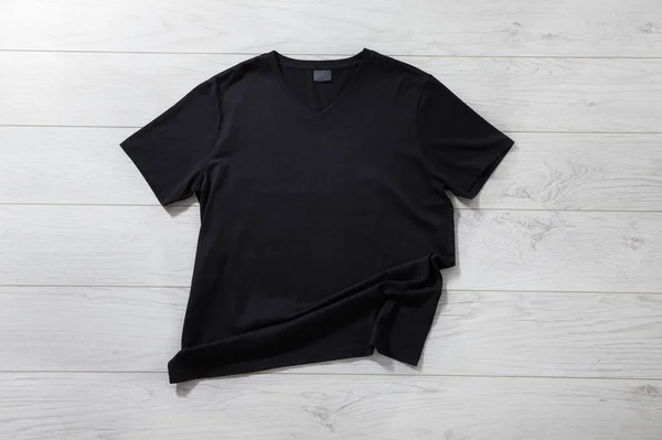 Black t-shirt on white wooden desk background. Mockup for design close up