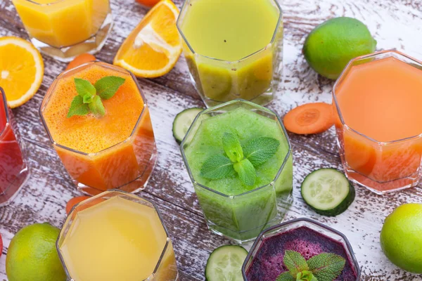many colorful freshly squeezed juices and fruits on a wooden board top view