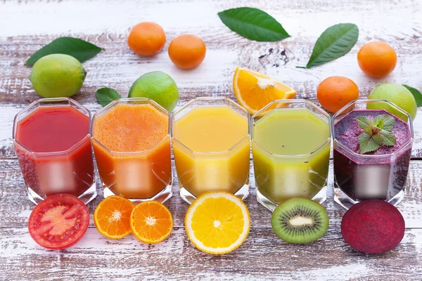 many colorful freshly squeezed juices and fruits on a wooden board top view