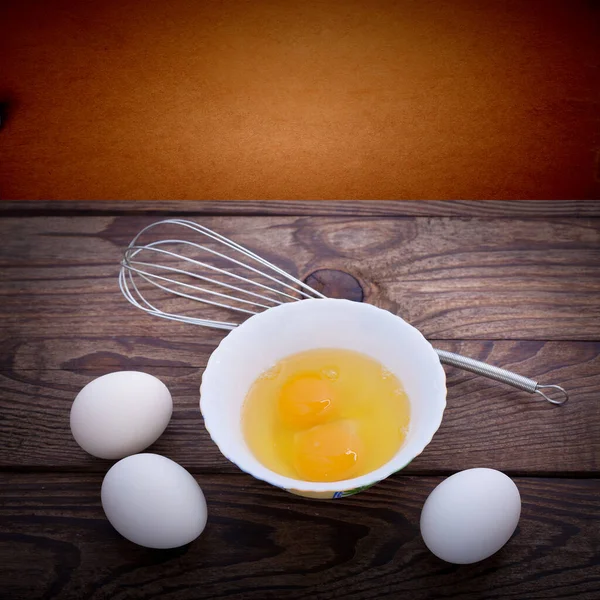 Egg in glass bowl and egg shells on wooden table. Baking ingredients, top view