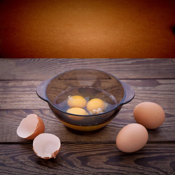 Egg in glass bowl and egg shells on wooden table. Baking ingredients, top view