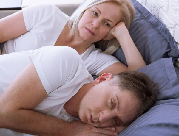 Middle aged woman covering ears while man snoring in bed. Concept intimacy after fifty