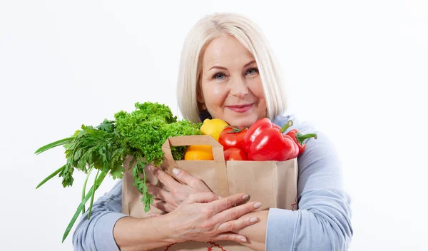金髪の幸せな女性は 美しい笑顔はビタミンと健康的な食事のために彼女の手の中に野菜やハーブ赤唐辛子と緑のレタスの袋を保持しています 健康的な食べ物の野菜をコンセプトに — ストック写真