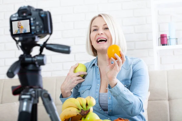 즐거운 여자는 스튜디오에서 카메라에 과일을 보여줍니다 스톡 사진
