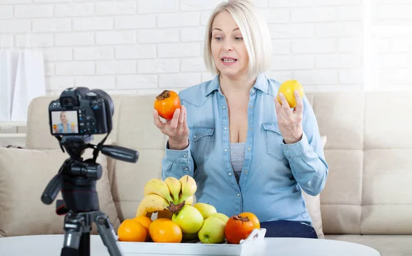 즐거운 블로거는 집에서 카메라에 과일을 보여줍니다 스톡 사진