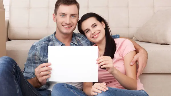 这对年轻漂亮的夫妇坐在新公寓的地板上 面带微笑 露出白纸 Videochat 图库图片