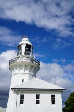 NSW Avustralya 'daki Sandy Cape Deniz Feneri manzaralı. Deniz feneri, bulutların ve mavi gökyüzünün arka planında güneşli bir günde sahil güzelliğini, deniz yolculuğunu ve kıyı sükunetini tasvir eder..