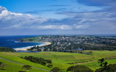 Kiama Tepeleri 'nden görülen bu çarpıcı kıyı manzarası, canlı mavi denizi, kumlu plajları ve dramatik gökyüzünün altında yemyeşil tepeleri, doğanın dingin güzelliğini yansıtıyor..