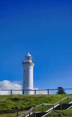 Kiama Avustralya 'da çarpıcı beyaz bir deniz fenerinin manzarası, çimenli bir yamaçta, tahta adımlarla ona doğru gidiyor.