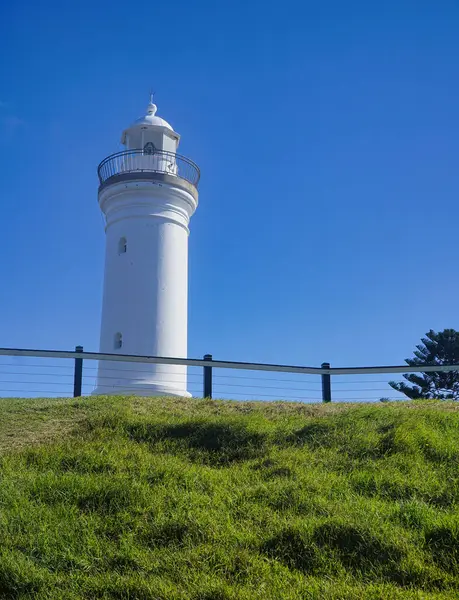 Bu fotoğraf, Kiama NSW Avustralya 'da çimenli bir yamaçta, parlak mavi gökyüzünde çarpıcı beyaz bir deniz feneri yakalar. Kiama Limanı Işığı