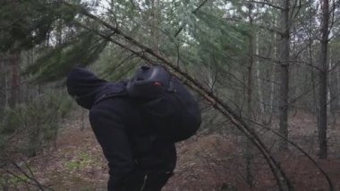 A man with a backpack bends down to pass under a bent tree