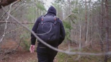 A young man, bending down, makes his way through the fallen trees that have closed the passage.