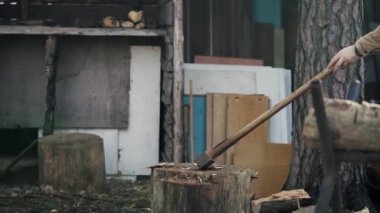 Genç bir adam ahırının yanında satırla odun kesiyor.