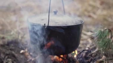 Toprağa gömülü bir çukurda kamp ateşinin üzerinde asılı duran dökme demir bir kazan.