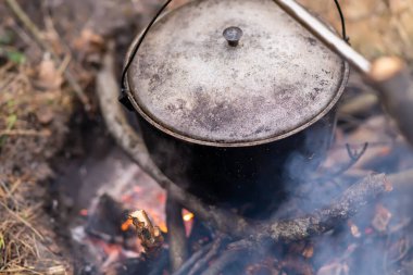 Top view of a cast iron pot with a lid hanging over a burning campfire