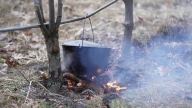 Walk by the campfire with food cooked on it in a cast-iron cauldron