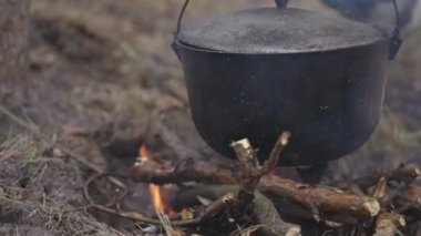 The tourist, putting his hand into the sleeve of the jacket, lifts the lid of the cauldron with food being prepared on an open fire.