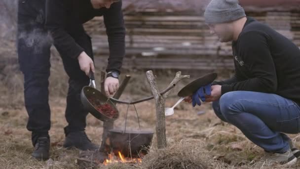 남자가 냄비와 프라이팬을 사용하여 불위에서 음식을 요리한다 — 비디오
