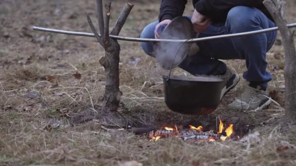 Молодий Чоловік Перемішує Їжу Великою Ложкою Котлі Звисає Над Вогнем — стокове відео