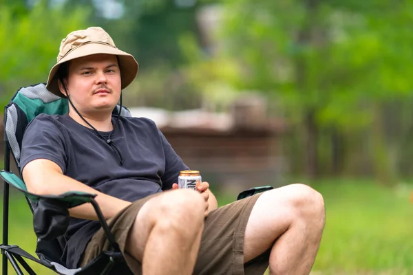 缶からビールを飲みながら屋外の椅子に座ってリラックスしている若い男 — ストック写真