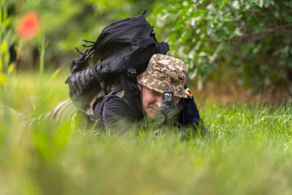 一个身穿军装 背着战术背包的人 以俯卧的姿势审视着他的来福枪的范围 — 图库照片