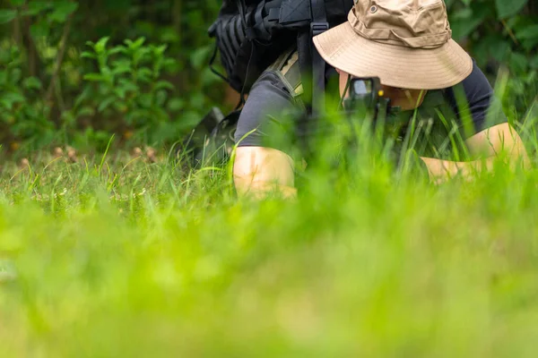 パナマの帽子を被った武装した男が草の上に横たわってライフルの範囲を調べる — ストック写真