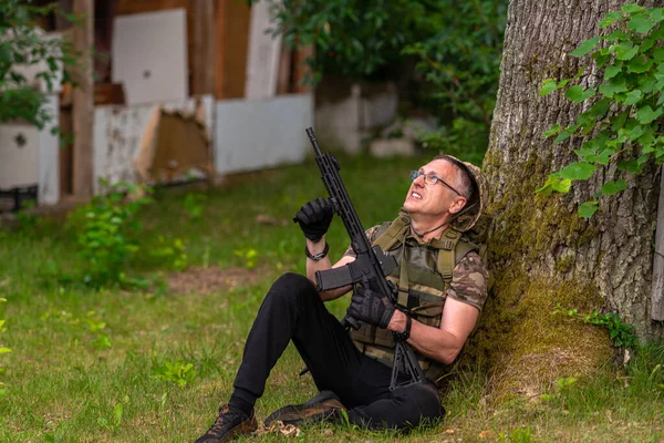 Человек Пистолетом Смотрит Вверх Держит Пулемет Наготове Прислонившись Дереву — стоковое фото