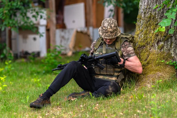Озброєний Чоловік Сидить Під Деревом Перевіряючи Свою Рушницю — стокове фото