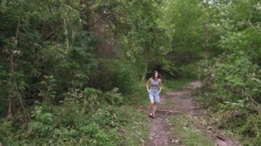 Bir kız, devrilmiş ağaçlarla bir ormanın içinden geçen bir yol boyunca geziniyor..