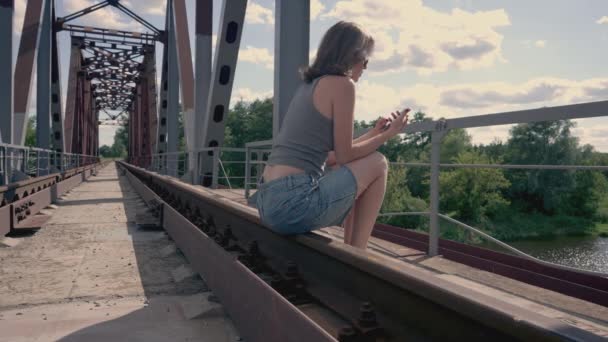 Flickan Sitter Järnvägsspåret Och Tittar Telefonen — Stockvideo