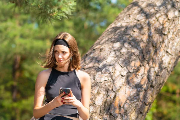 Una Chica Cerca Árbol Sostiene Teléfono Sus Manos Mira Con — Foto de Stock
