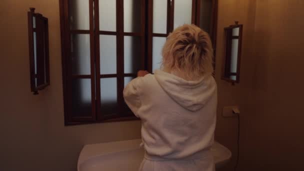 一个穿着毛茸茸的白袍的女人走进浴室 打开窗户 — 图库视频影像