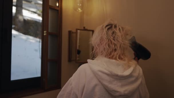 一个女人在窗前的浴室里用吹风机吹干她的头发 — 图库视频影像