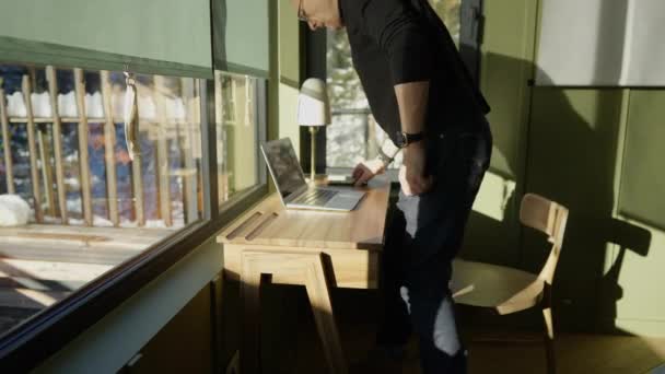 一个男人坐在写字台前 手里拿着笔记本电脑 手机在上面 — 图库视频影像