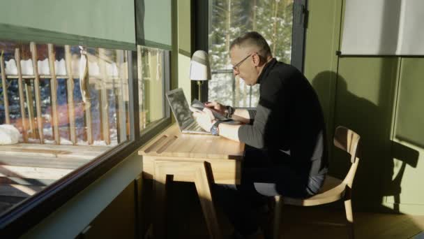 一个男人在他的书桌上翻阅一本书 书桌上有一台笔记本电脑和一部电话 — 图库视频影像