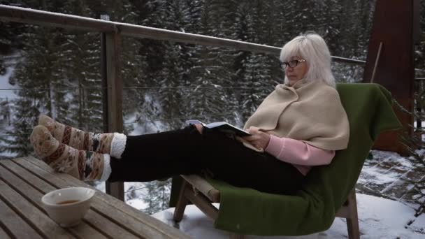 Під Легким Снігом Жінка Трикотажних Шкарпетках Окулярах Сидить Терасі Читає — стокове відео