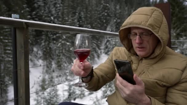 Мужчина Смотрит Телефон Пьет Красное Вино Сидя Фоне Зимнего Леса — стоковое видео