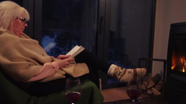 Женщина Сидящая Кресле Перед Камином Начинает Читать Книгу Зимним Вечером — стоковое видео