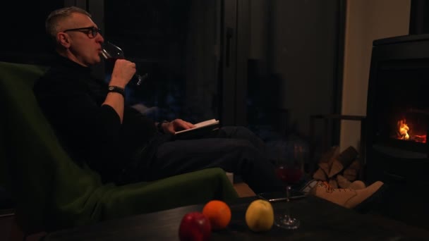 Mężczyzna Pije Grzane Wino Czyta Książkę Siedząc Wygodnie Krześle Przed — Wideo stockowe