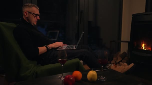 Mężczyzna Fotelu Używa Laptopa Siedząc Krześle Przed Kominkiem Swojej Chatce — Wideo stockowe