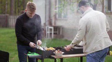 İki adam ızgarada et ve patates pişiriyor.