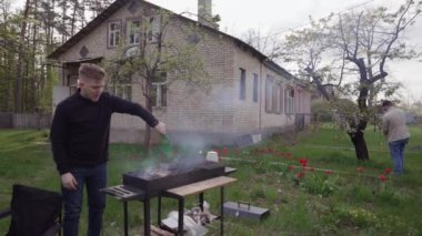 İki adam ızgarada yemek pişiriyor ve evlerinin arka bahçesindeki ağaçla ilgileniyorlar..