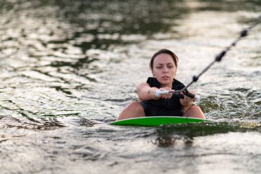 Wakeboard 'daki genç bir kadın suyun içindeyken bir teknenin ipine tutunuyor..