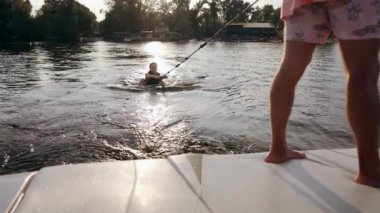 Kız suyun içinde ve bir wakeboard 'a binmeye çalışıyor, eğitmenin talimatlarını dinliyor..