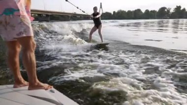 Bir wakeboardcu bir nehirde idman yapıyor, elinde bir halatla motorlu bir tekneye tutunuyor.