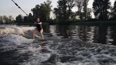 Nehirde, bir atlet kayığa bağlı halatı tutarken wakeboard yapar..
